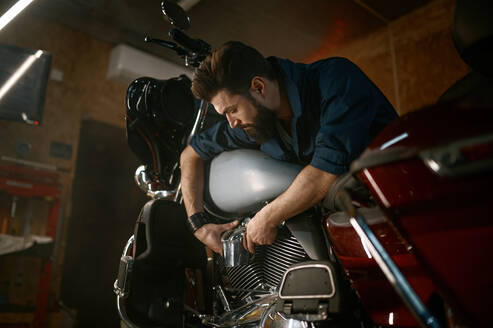 Male mechanic working in garage and repairing custom motorcycle. Creative authentic workshop concept. Male mechanic working in garage and repairing custom motorcycle - INGF12224