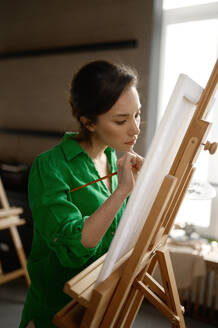 Inspired and concentrated young female student having classes at art studio. Closeup woman artist painting on canvas at workshop. Inspired and concentrated young female student having classes at art studio - INGF12227