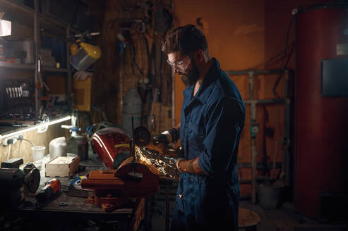 Techniker bei der manuellen Herstellung und Montage eines Ersatzteils in der Werkstatt. Technikerhand und Funkenflug von der Maschine. Techniker bei der manuellen Herstellung und Montage eines Ersatzteils in der Werkstatt - INGF12237