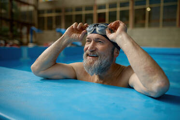 Gesunder älterer Mann schwimmt im Hallenbad und genießt den sportlichen Lebensstil und den aktiven Ruhestand - INGF12242