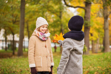 Childhood, season and people concept - smiling little girl and boy with autumn leaves in park - INGF12256