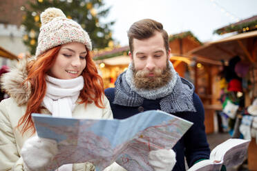 Holidays, winter, christmas, tourism and people concept - happy couple in warm clothes with map and city guide in old town - INGF12257