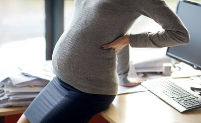 Pregnancy, business, work and people concept - pregnant businesswoman sitting on table at office. pregnant businesswoman sitting on table at office - INGF12258