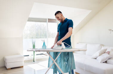 Housework and household concept - man ironing shirt on iron board at home. man ironing shirt by iron at home. man ironing shirt by iron at home - INGF12286