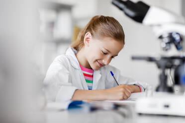 Education, science and children concept - girl studying chemistry at school laboratory and writing to workbook. girl studying chemistry at school laboratory - INGF12288