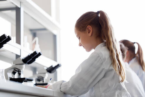 Education, science and children concept - girl studying chemistry at school laboratory and writing. girl studying chemistry at school laboratory - INGF12289