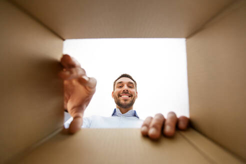 Mail delivery and surprise concept - smiling man taking something out of parcel box, from below. smiling man taking something out of parcel box - INGF12296