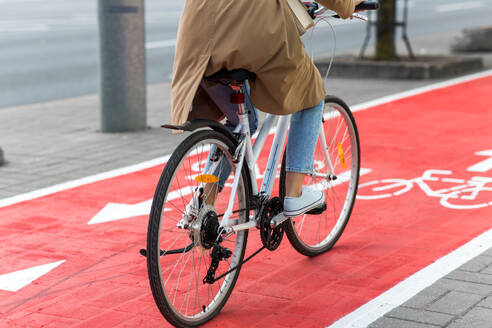 Traffic, city transport and people concept - woman cycling along red bike lane with signs of bicycles on street. woman cycling along red bike lane road in city - INGF12298