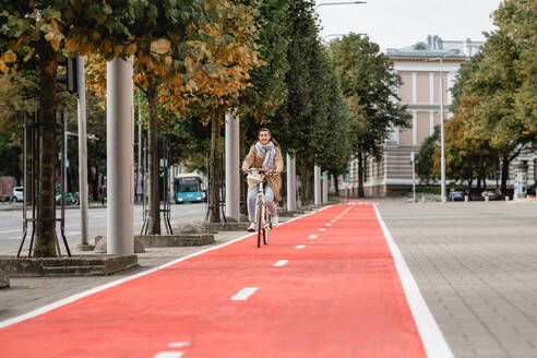 Traffic, city transport and people concept - happy smiling woman riding bicycle along red bike lane or two way road on street. woman riding bicycle along red bike lane in city - INGF12299