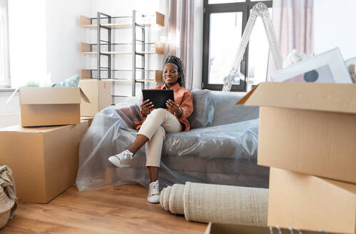 Moving, people and real estate concept - happy smiling woman with tablet pc computer and boxes at new home. smiling woman with tablet pc moving into new home - INGF12339