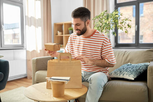 Consumption, eating and people concept - smiling man unpacking takeaway food in paper bag at home. smiling man unpacking takeaway food at home - INGF12343