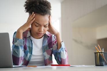 Tired african american teenage schoolgirl suffer headache while doing homework at laptop at home. Exhausted, frustrated teenager girl worried about educational problem or bullying. Difficult elearning. Tired african american teen girl suffer headache doing homework at laptop. Difficult elearning - INGF12358