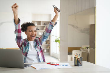 Excited happy african american girl student got good exam test scores on laptop. Overjoyed teenage schoolgirl raising hands screaming celebrates personal achievement or finishing homework.. Overjoyed african american student teen girl got email with good exam scores, celebrates success - INGF12359