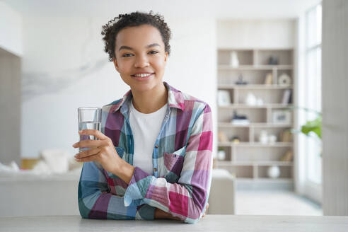 Happy african american girl drinks pure water from a glass. Gorgeous young woman has mineral water at home. Weight loss dieting, refreshing and detox. Healthy lifestyle, morning health routine.. Happy african american girl drinks water from a glass. Healthy lifestyle, morning health routine. - INGF12362
