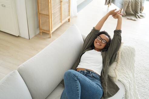 Lazy weekend morning of teenager. Carefree african american girl is relaxing on couch and pillow at her apartment. Young afro woman is stretching and smiling. Leisure and rest concept.. Carefree african american girl is relaxing on couch and pillow at her apartment. Leisure concept. - INGF12384