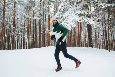Optimistischer junger Mann in warmer Winterkleidung hat Spaß im Freien im Winterwald gekleidet - INGF12409