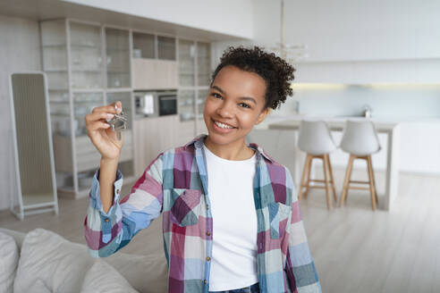 Young biracial girl homeowner tenant showing key to new house, rented or purchased apartment. African american female owner holding bunch of keys standing in modern flat. Relocation, real estate rent.. Happy young biracial girl homeowner tenant shows key to new house. Relocation, real estate rent - INGF12437