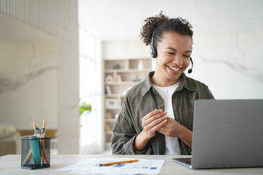 Happy student has online lesson from home. Distance study on quarantine. Young woman in headset gives consultation. African american manager is smiling. Remote work of an operator of support service.. Happy student has online lesson. Distance study on quarantine. Young african woman in headset. - INGF12447