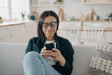 Happy woman relaxing and surfing through internet with mobile phone. Girl is texting and smiling, receiving messages. European lady enjoying time at home. Chatting, gadget and application using.. Happy woman is chatting on phone at home. Girl is texting and smiling, receiving messages. - INGF12466