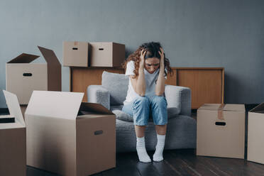 Tired european woman sitting among packed boxes. Girl is upset with moving. Hopeless young lady in jeans and white t-shirt getting in trouble. Depression and bankruptcy concept.. Tired european woman sitting among packed boxes. Hopeless young lady getting in trouble - INGF12506