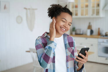 Modern young mixed race girl enjoys her music, holding a smartphone and using musical apps to enhance her home listening experience. - INGF12537