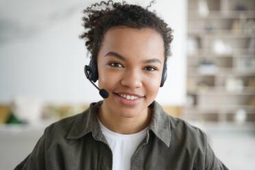 Engaged in distance education, a smiling mixed race girl student wearing a headset looks directly at the camera, embracing e-learning. - INGF12545