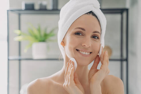 Hispanische Frau nach dem Duschen: Reinigung der Haut, Abschminken mit Wattepads. Hautpflegeroutine. - INGF12547