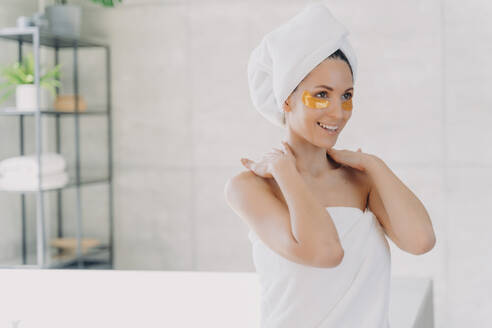 Woman with eye patches enjoys skincare routine in bathroom after shower. - INGF12551