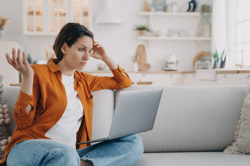 Eine verwirrte Frau auf dem Sofa hat Probleme mit ihrem Laptop, einem Virus oder schlechtem Internet. Eine empörte Frau sieht sich eine Serie an und ist über die Filmhandlung empört. - INGF12562