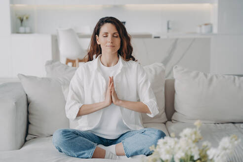 Spanish woman relaxes in lotus pose at home. Yoga, meditation, stress reduction - INGF12568