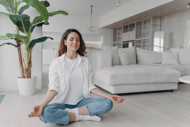 Serene hispanic woman practices yoga in living room. Meditation, breathing exercises, wellness at home. - INGF12569