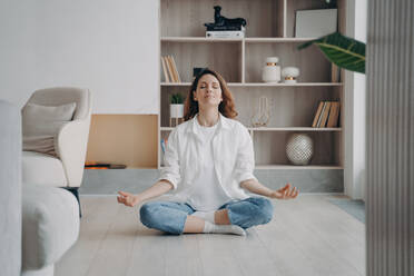Calm woman in lotus position, meditating in living room. Yoga, fresh air, alone at home. Recreation, wellness. - INGF12570