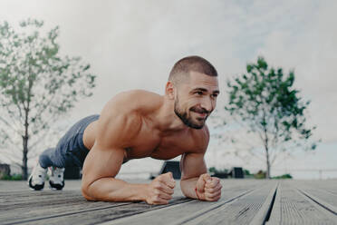 Fit bearded man in plank pose, smiles outdoors. Focuses on health and fitness. - INGF12590