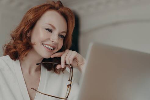 Focused ginger copywriter in close-up, preparing web publication, watching webinar, wearing spectacles, concentrated on remote job. - INGF12613