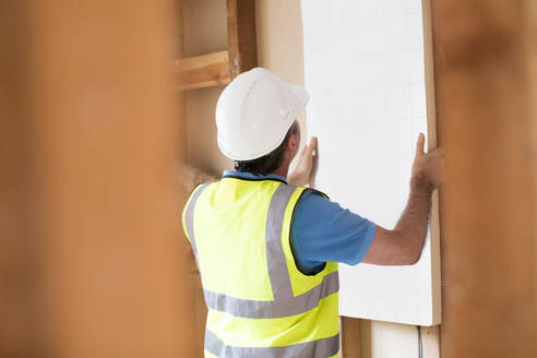 Builder Fitting Insulation Boards Into Roof Of New Home - INGF12642