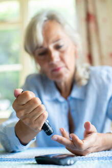 Senior Diabetic Woman Testing Blood Sugar Level At Home - INGF12657