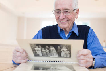 Senior Man At Home Looking At Photo Album - INGF12658