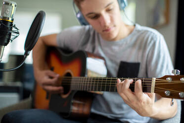 Teenage Boy Playing Guitar And Recording Music At Home - INGF12661