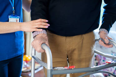 Close Up Of Senior Man With Hands On Walking Frame Being Helped By Care Worker - INGF12663