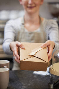 Close Up Of Female Worker in Cafe Serving Meal In Sustainable Recyclable Packaging With Wooden Fork - INGF12676