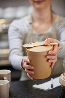 Close Up Of Female Worker in Cafe Serving Meal In Sustainable Recyclable Packaging With Wooden Spoon - INGF12677