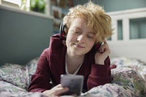 Teenage Girl Wearing Wireless Headphones Listening To Music Steaming From Mobile Phone At Home - INGF12680