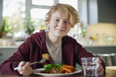 Portrait Of Teeange Girl Eating Vegan Meal Sitting At Table In Kitchen At Home - INGF12698