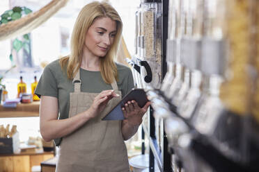 Female Owner Of Sustainable Plastic Free Grocery Store Checking Stock On Shelves - INGF12708