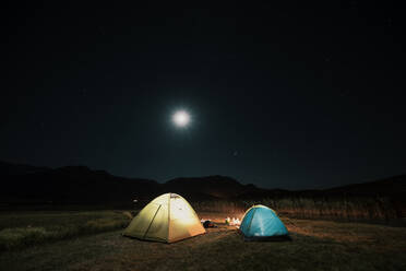 Camping in the mountains under the moon. A tent pitched up and glowing under the sky.. Tourist tents in camp among meadow in the night mountains - INGF12735