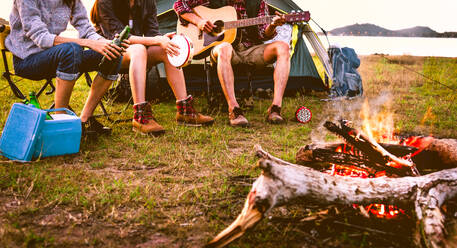 Travelers camping doing picnic and playing music in meadow field. Mountain and lake background. People and lifestyles concept. Outdoors activity and leisure theme. Backpacker and Hiker lifestyle - INGF12777