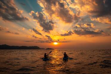 A female and a male sailing with canoes close to each other at sunset. Female and a male sailing with canoes close to each other at sunset - INGF12811