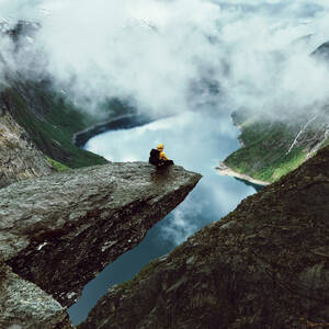 Man sits at the end of Trolltunga before the mountains - INGF12815