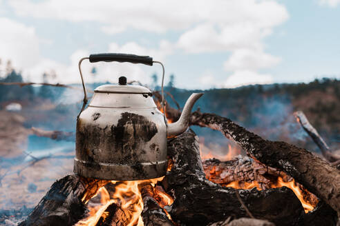 Boiling water on a camping trip with fire in the mountains, cooking on a fire with firewood. Kettle on fire. Picnic. Kettle on fire in the mountains wallpaper - INGF12817