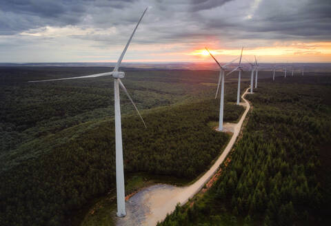 Wind turbine farm on beautiful forest landscape at sunset. Renewable energy production for green ecological world. Aerial view of wind mills farm park on evening mountain . . Wind turbine farm on beautiful forest landscape at sunset. Renewable energy production for green ecological world. Aerial view of wind mills farm park on evening mountain. - INGF12832